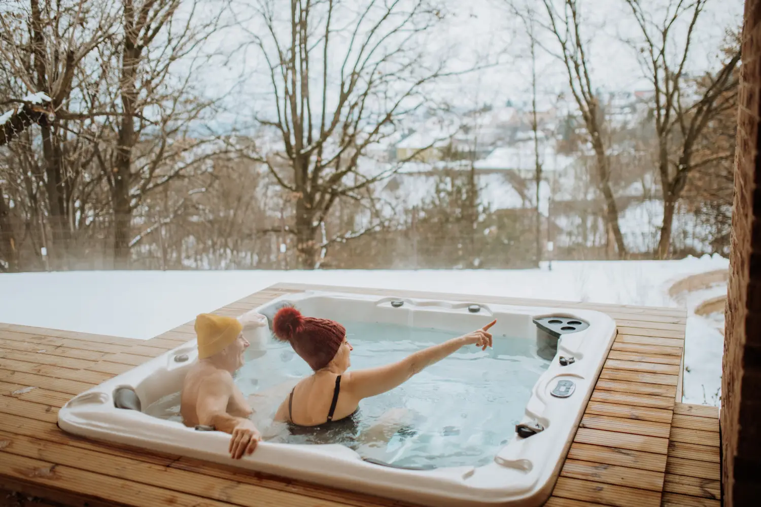 Senior couple in kintted cap enjoying together outdoor bathtub and view at their terrace during cold winter day.
